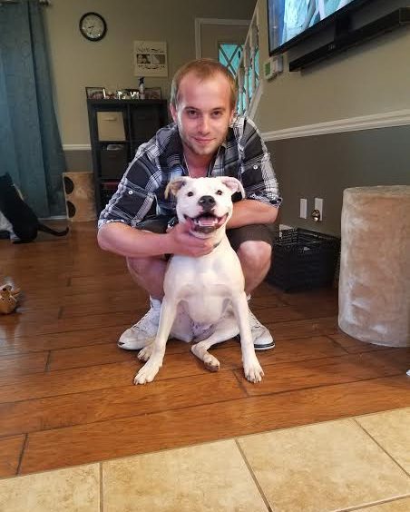 A man kneeling down next to a white dog in a living room.