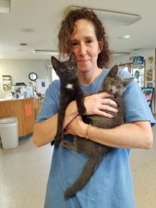 A woman holding two black kittens in a room.