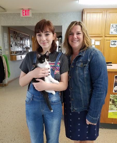 Two women standing next to a black and white cat.