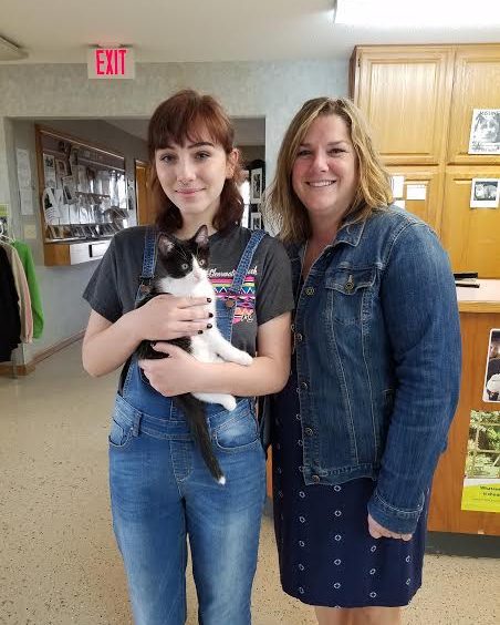 Two women standing next to a black and white cat.