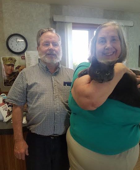 An older man and woman holding a black cat.
