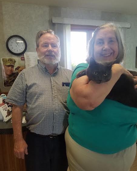 An older man and woman holding a black cat.