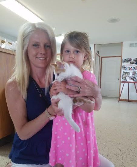 A woman holding a white cat and a little girl.