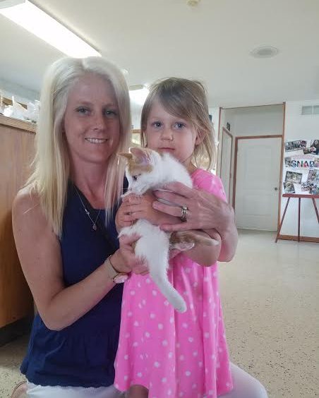 A woman holding a white cat and a little girl.