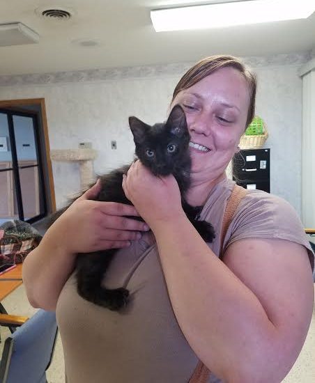 A woman holding a black kitten in her arms.