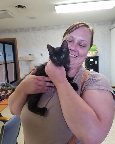 A woman holding a black kitten in her arms.