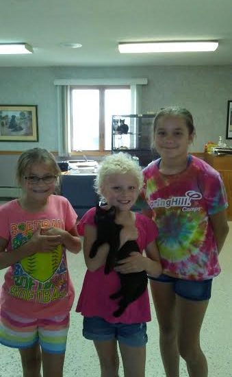 Three girls posing for a picture with a black cat.