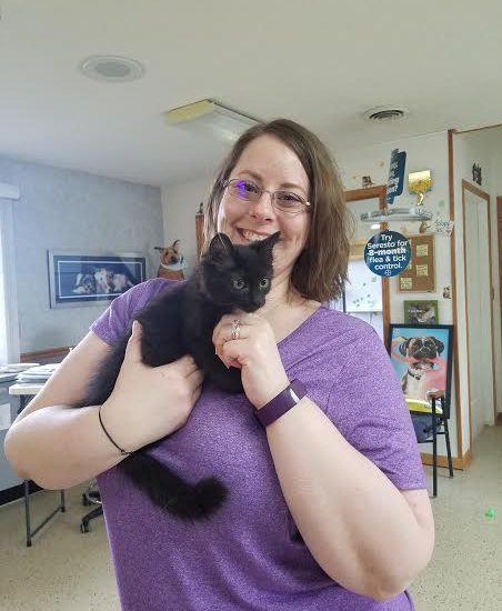 A woman in a purple shirt holding a black cat.