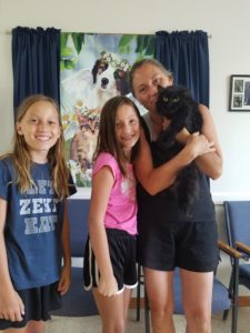 A woman and her two daughters holding a black cat