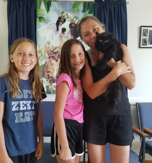 A woman and her two daughters holding a black cat