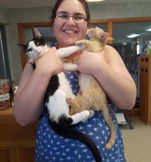 A woman holding two cats in her arms.