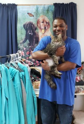 A man holding a cat in front of a rack of clothes.