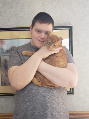 A young man holding an orange tabby cat.
