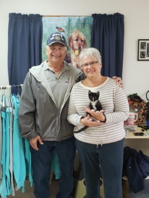 A man and woman standing next to a cat in a clothing store.