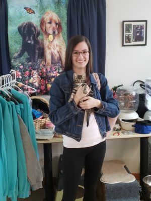 A woman holding a kitten in a room full of clothes.